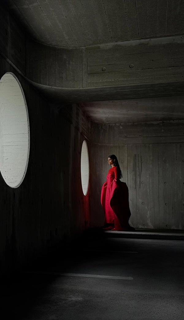 Женщина в длинном красном платье стоит в пустой комнате, пока ее фотографируют. Приложение «Фото» переключает фокусные расстояния, чтобы продемонстрировать возможности профессиональной камеры: 35 мм