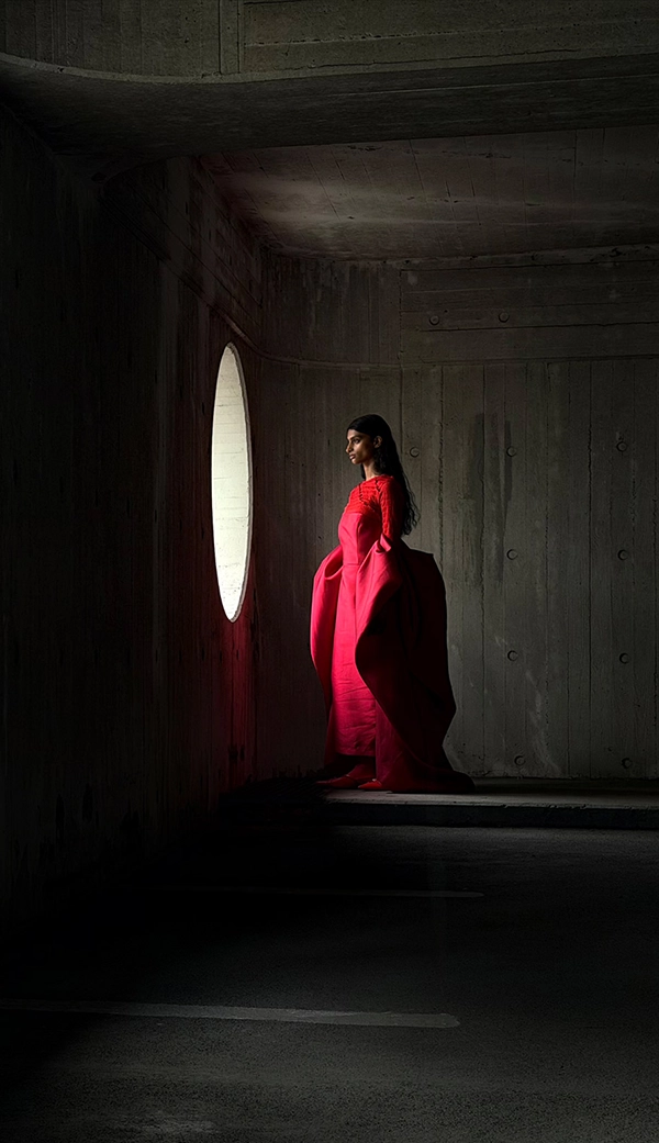 Женщина в длинном красном платье стоит в пустой комнате, пока ее фотографируют. Приложение «Фото» переключает фокусные расстояния, чтобы продемонстрировать возможности профессиональной камеры: 48 мм